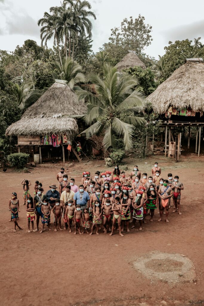 Aerial view of indigenous people in traditional attire gathered in a rural village setting.